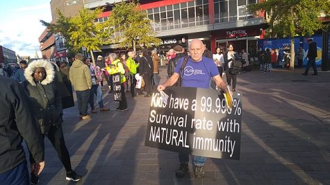 Anti-vaccine protester carrying a large black board which reads Kids have a 99.99% survival rate with NATURAL immunity. The protesters were handing out leaflets to passers-by and put up signs on the construction fences outside Santander bank.