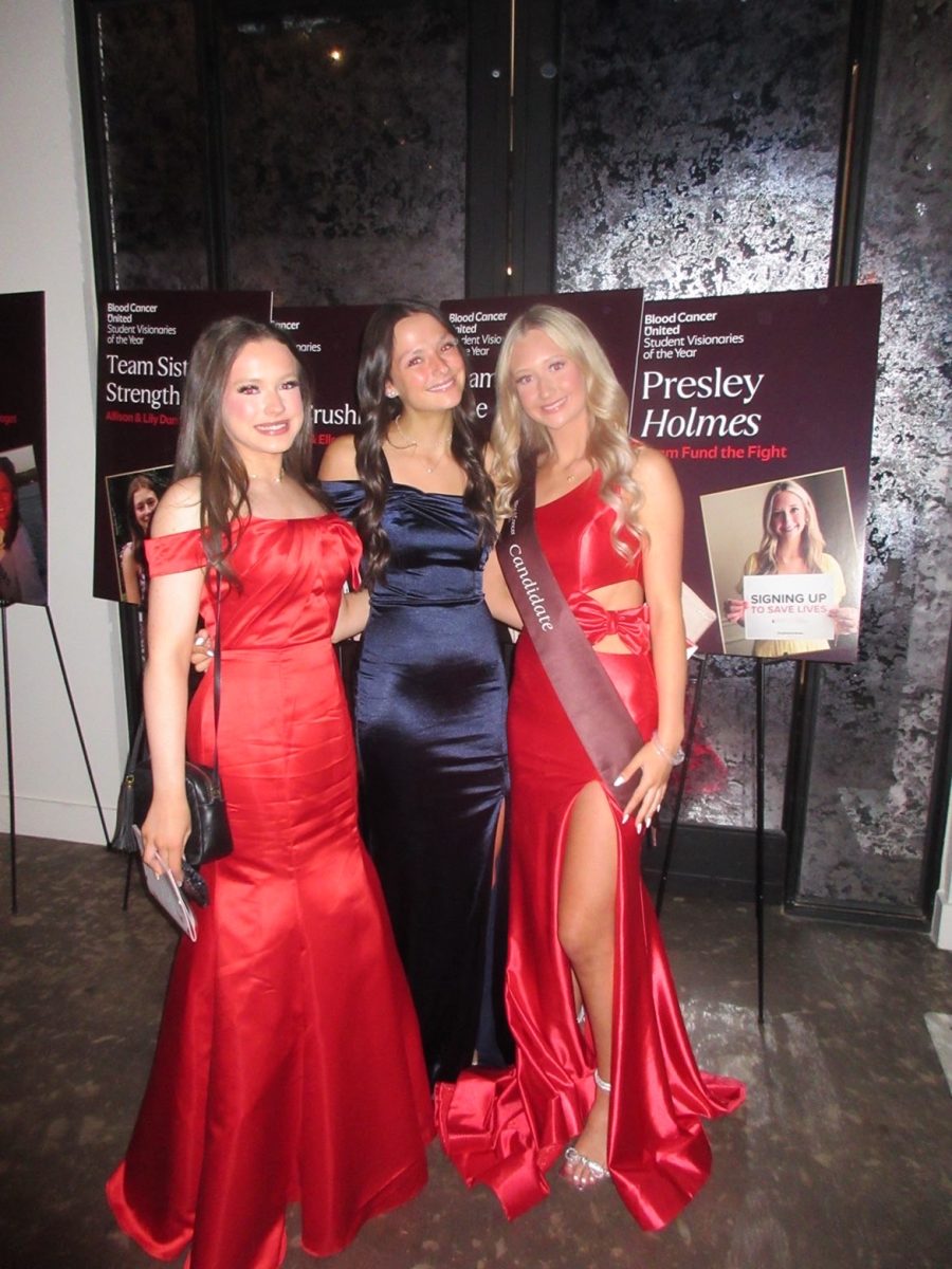 Mackenzie Pogar, Ainsley Capri, and Presley Holmes all at the Blood Cancer United Gala taking a photo by Presley Holmes' candidate poster. Photo provided by Mackenzie Pogar, used with permission.